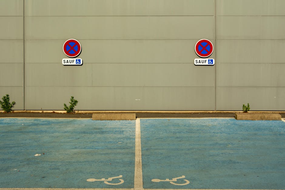 Photograph showing a vertical metal street sign mounted on a pole alongside a red brick building in Southgate, with a clear sky in the background. The top part of the sign has a white background with a red circle and diagonal line indicating no parking or stopping, along with a black van icon beneath, signifying restrictions for vehicle parking during certain times. Below, a green circle with a white 'P' indicates designated parking, specifying a maximum stay of two hours from 8 am to 6 pm, Monday to Friday. The sign is situated on a paved sidewalk, with moving traffic and parked cars visible in the background, highlighting urban street parking rules relevant for house removals or furniture transport in Southgate. The sign's clear visibility supports understanding parking regulations necessary for planning and executing property relocations in the area.